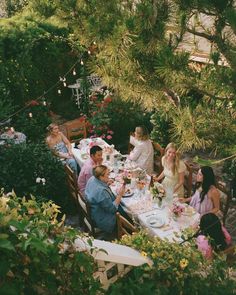 a group of people sitting around a table eating food and drinking wine in the garden