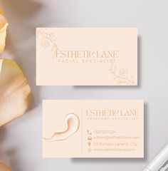 two business cards sitting on top of a desk next to a pen and flower arrangement