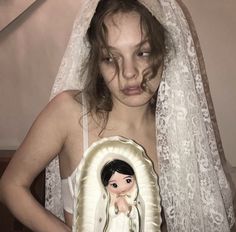 a woman wearing a veil and holding a doll in front of her face with an image on it