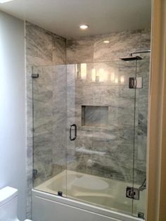 a white toilet sitting next to a shower in a bathroom with marble walls and floor