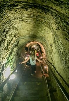 two people are walking up some stairs in a tunnel with lights on them and one person is holding onto the handrail