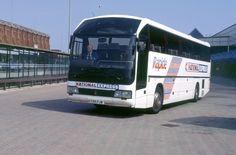 a white bus parked in front of a building on a brick road next to tall buildings