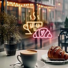 a cup of coffee next to a croissant on a table with a neon sign in the background