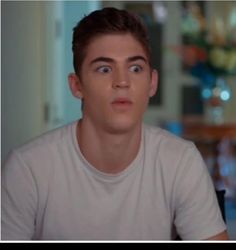 a young man sitting in front of a table looking at the camera with an intense look on his face