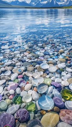 many different colored rocks are on the shore of a lake with mountains in the background