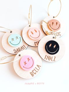 four personalized wooden ornaments with smiley faces and names hanging from strings on a white background