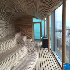 a room with wooden flooring and walls next to a balcony overlooking the ocean on a sunny day