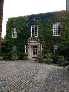 an old building covered in vines and flowers on a cobblestone street with potted plants