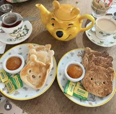 a winnie the pooh teapot sits on a table next to some breakfast foods