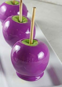 three purple apples sitting on top of a white plate with wooden sticks in each one