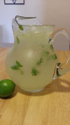 a pitcher filled with limeade sitting on top of a wooden table next to a lime