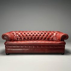 a red leather couch sitting on top of a white floor next to a gray wall