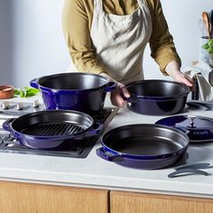 a woman in an apron is cooking on the stove with blue pots and pans