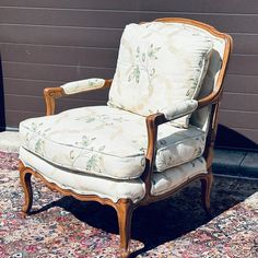 an old chair sitting on top of a rug next to a building with a wall in the background