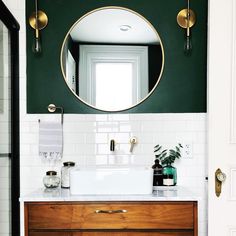 a bathroom with green walls and white tile on the floor, along with a wooden vanity topped with a round mirror