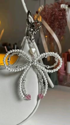 a white purse with pearls on it and a bow charm hanging from the front pocket