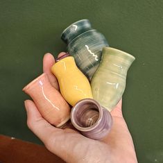 a hand holding several different colored vases