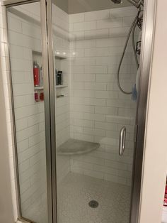 a walk in shower sitting next to a white tiled wall and floor with a glass door