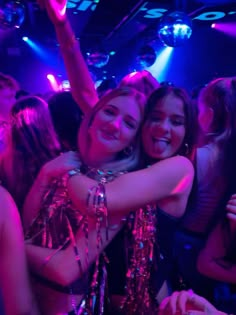 two girls hugging each other at a party with disco lights on the ceiling behind them