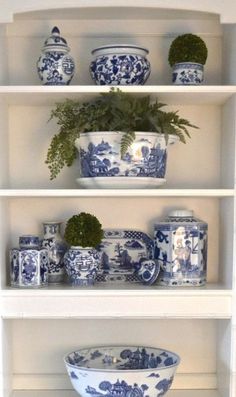 a white shelf with blue and white vases on it's shelves next to a potted plant