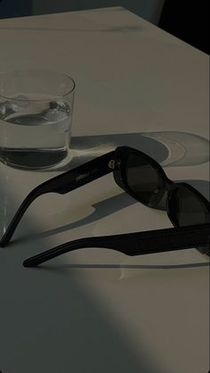 a pair of black sunglasses sitting on top of a table next to a glass of water