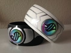 two white and black bracelets with colorful designs on them sitting on a table next to each other