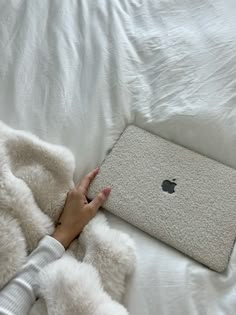 a woman laying in bed with an apple laptop on her lap and she is holding the cover