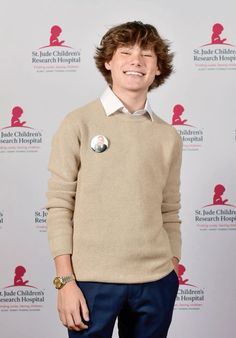 a young man wearing a sweater and blue pants smiles at the camera while standing in front of a white backdrop