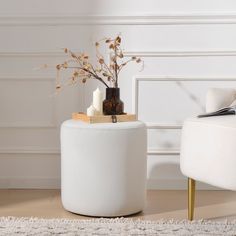 a white stool with a vase on top and some flowers in the middle sitting next to it