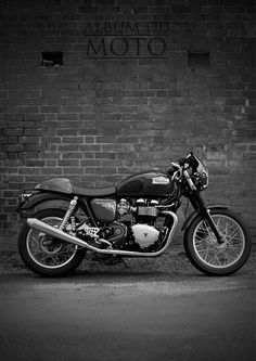 a black and white photo of a motorcycle parked in front of a brick wall with the word moto written on it