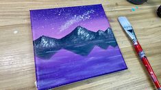 an acrylic painting of mountains and the night sky with stars above them on a wooden table