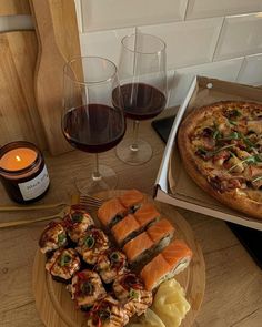 two pizzas and some appetizers on a table with glasses of red wine