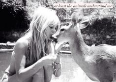 a woman sitting on the ground next to a deer with her hand in her mouth