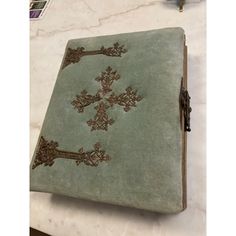 an old book is sitting on a marble counter top, with ornate designs in gold and green