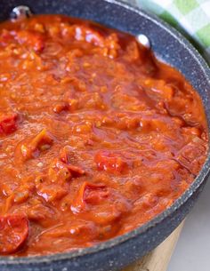 a pan filled with red sauce on top of a wooden cutting board