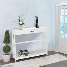 a white table with a book and vase on it in front of a blue wall