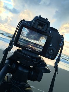 a camera that is sitting on a tripod near the water's edge at sunset