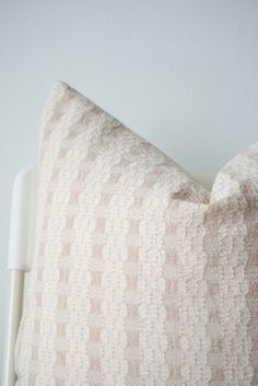 a close up of a pillow on a white bed with a light colored wall in the background