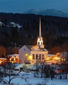 a church lit up with christmas lights in the snow at night, surrounded by trees and mountains