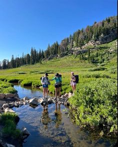 three hikers cross a stream in the mountains