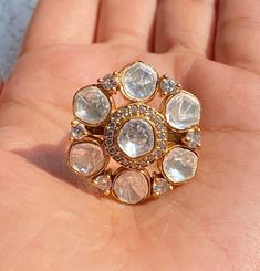 a hand holding a gold ring with white stones and clear crystals on it's sides