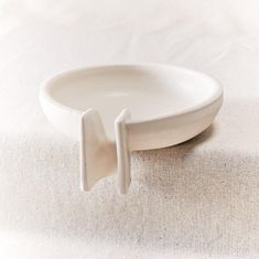 a white bowl with two handles on top of a cloth covered tablecloth, sitting on a plain surface