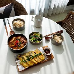 a table topped with bowls filled with food next to a plate of rice and chopsticks