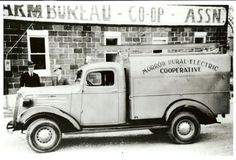 an old truck parked in front of a brick building with two men standing next to it