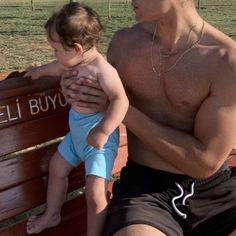 a man holding a baby sitting on top of a wooden bench next to a field