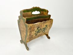 an old wooden box with green and gold designs on the front, sitting on a white surface