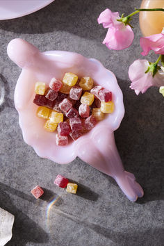 a pink bowl filled with gummy bears on top of a table next to flowers