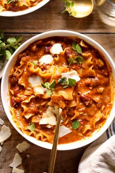 two bowls filled with pasta and sauce on top of a wooden table next to utensils