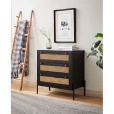 a black dresser with wicker drawers in front of a white wall and wooden ladder