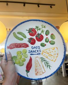 a person holding up a paper plate that says dad's snacks and vegetables on it